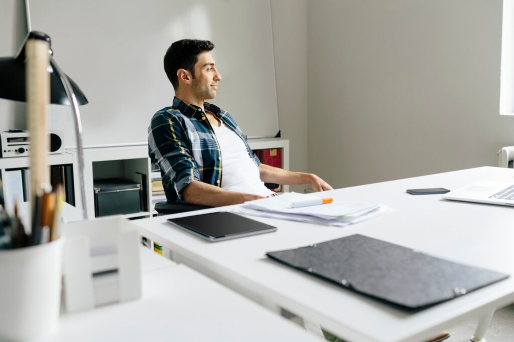 Young man with tablet and notes at desk in office thinking