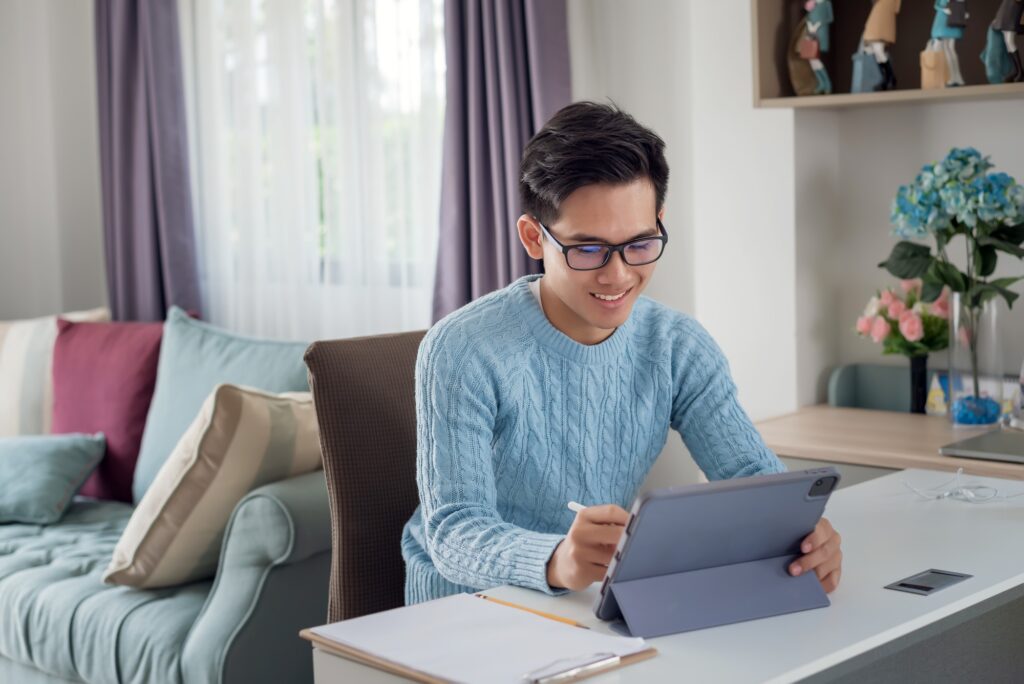 Young Asian man happy working at home using a tablet.