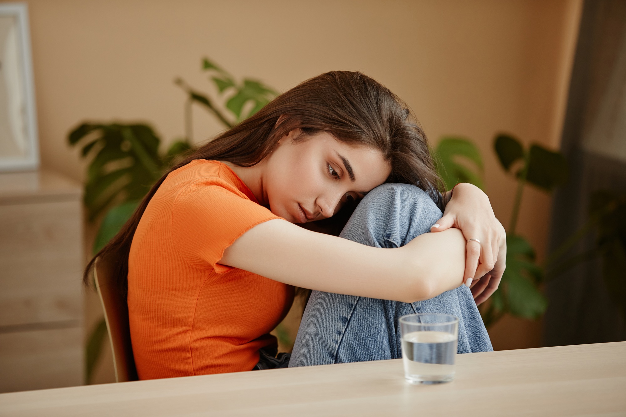 Depressed young woman struggling with mental health issues curled up on chair